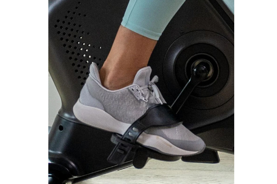 Gray and white knit sneaker with white sole worn by person on Schwinn upright exercise bike pedal