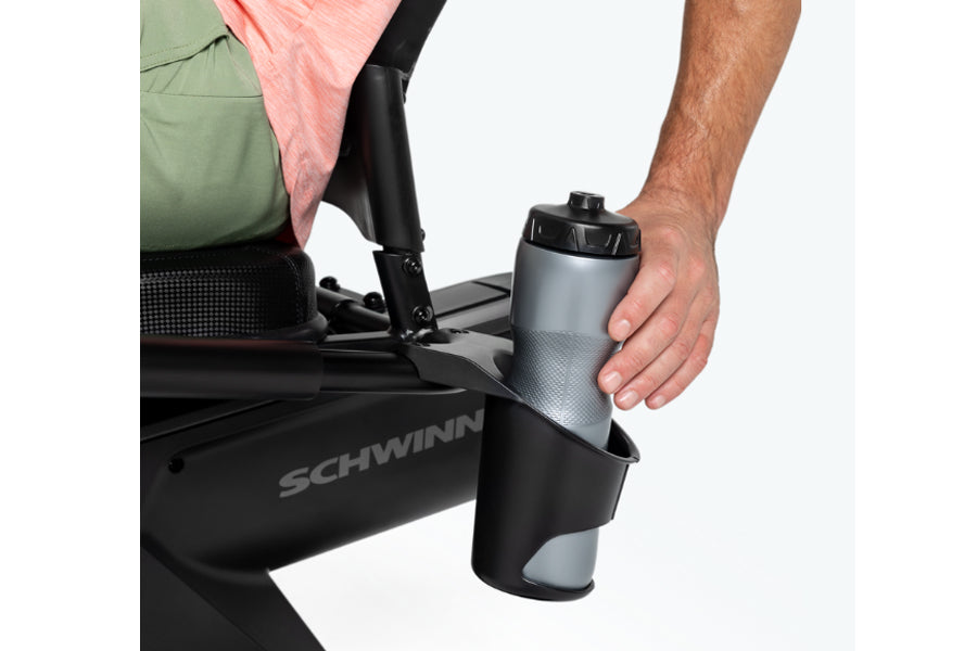Man holding gray and black water bottle on Schwinn 290 recumbent exercise bike, worn by model