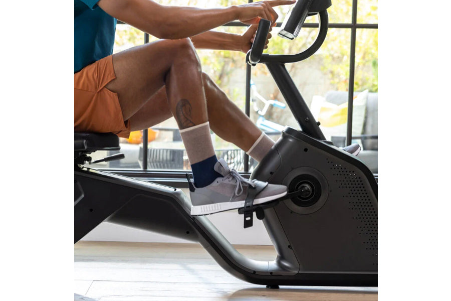Person wearing orange shorts and navy crew socks riding black Schwinn 290 recumbent exercise bike indoors