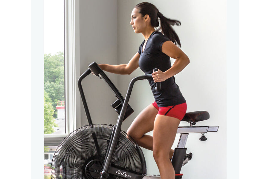 Woman wearing navy sports top and red shorts using black Schwinn Airdyne AD7 exercise bike with large fan wheel