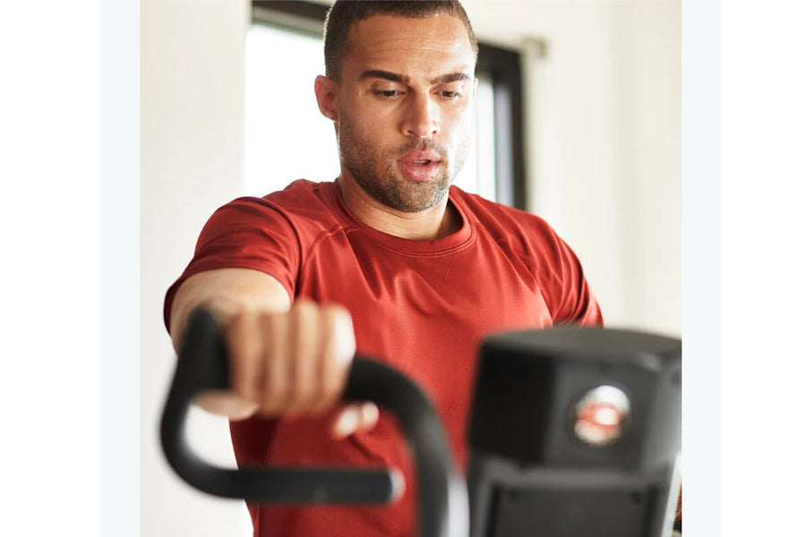 Man wearing red t-shirt using black Schwinn Airdyne AD7 exercise bike indoors