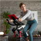 Woman using black and red Schwinn IC4 indoor cycling bike with red tablet holder, wearing gray long-sleeve top and teal leggi