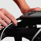 Hand plugging charging cable into black indoor exercise bike with digital display