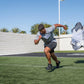 Man wearing gray shirt and black shorts using white and black resistance parachute while running on grass field