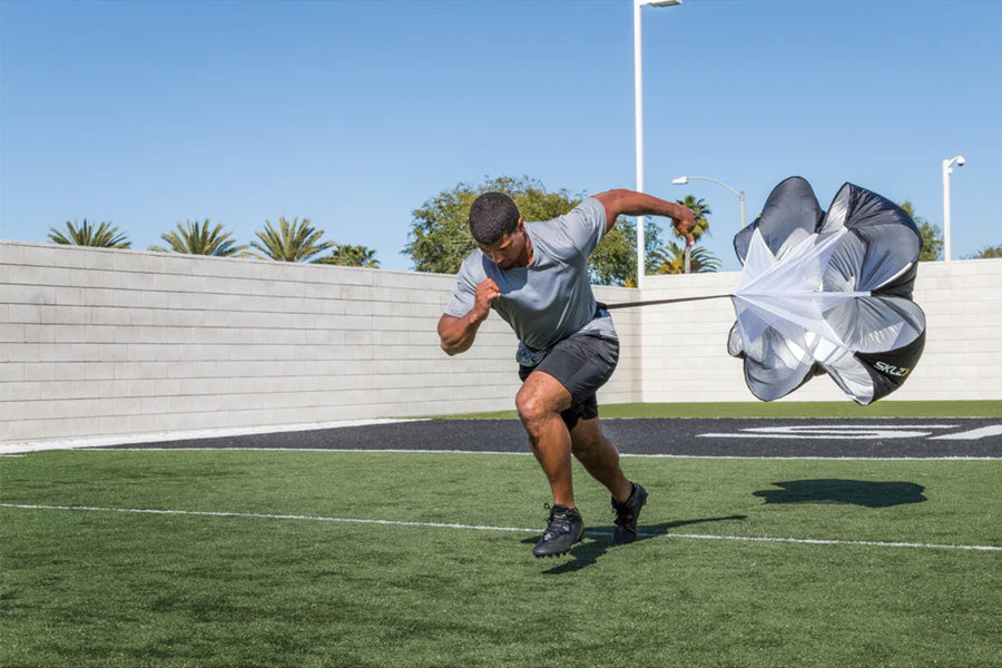 Man wearing gray shirt and black shorts using white and black resistance parachute while running on grass field