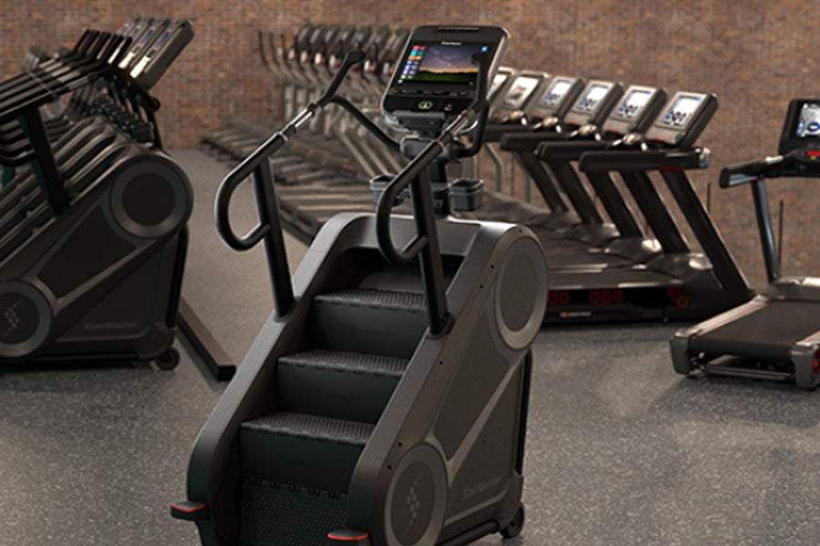 Black and silver StairMaster 8Gx stair stepper with digital display in gym setting surrounded by dumbbells and equipment