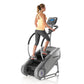 Woman using gray StairMaster SM3 StepMill cardio machine with digital display, wearing yellow tank top and black capris