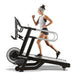 Woman in light blue tank top and black shorts running on black HIITMill treadmill with silver handles against white backgroun