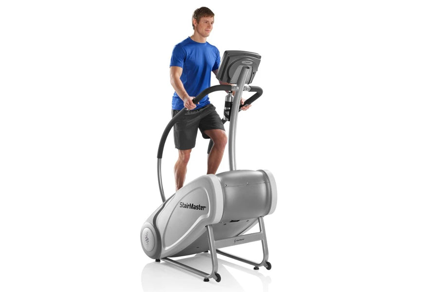 Man wearing blue t-shirt and black shorts using gray StairMaster SM3 StepMill exercise machine with digital display on white 