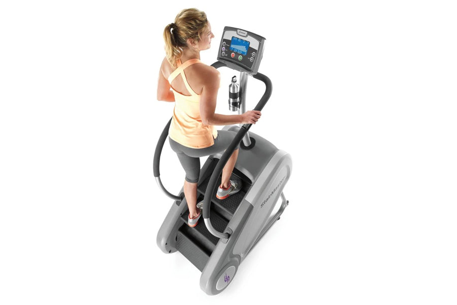 Woman in yellow tank top using gray StairMaster StepMill with digital console display, overhead view