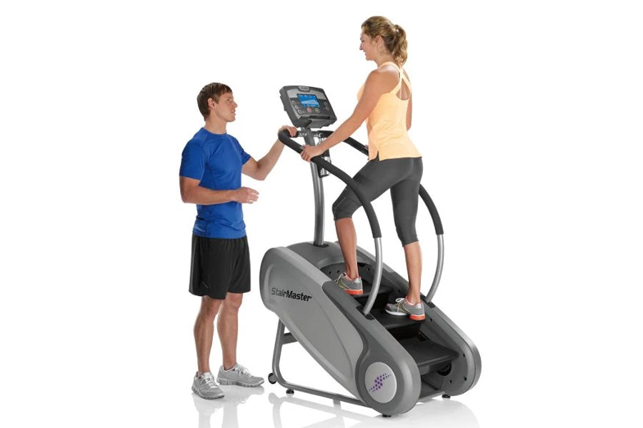 StairMaster SM3 StepMill with digital display, shown with woman exercising and man standing beside it on white background