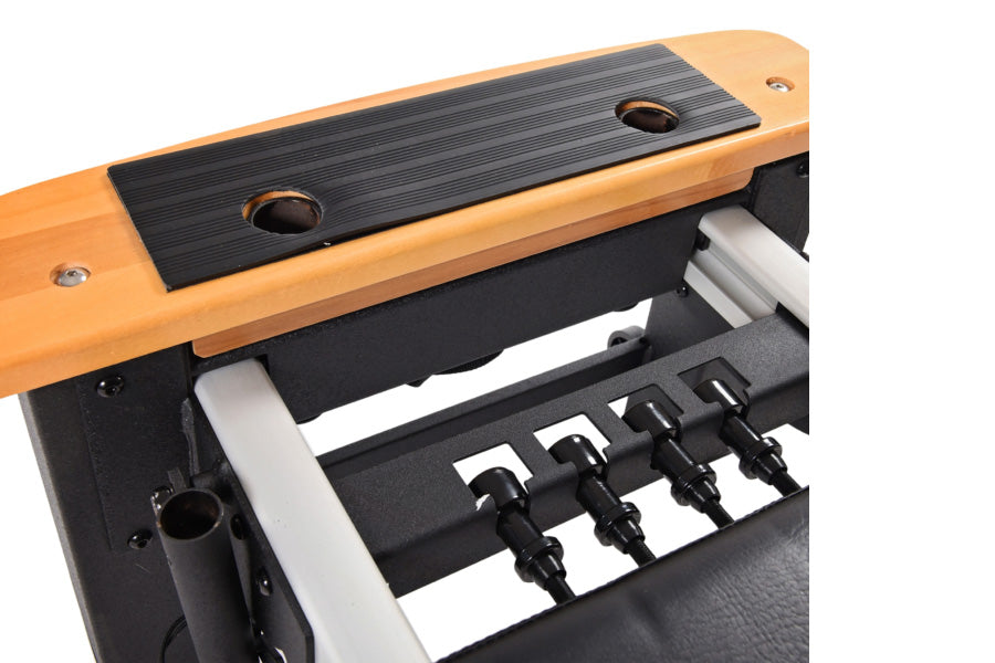 Stamina Pilates Reformer with natural wood frame, black rubber foot platform, and black metal springs on white background
