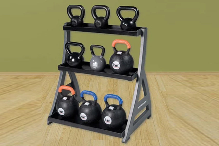 Three-tier kettlebell rack with gray steel frame and black shelves holding nine black kettlebells with colored handles, on wo
