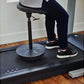 Black and white sneaker worn by model standing on treadmill desk with circular base, adjustable stand, and gray countertop
