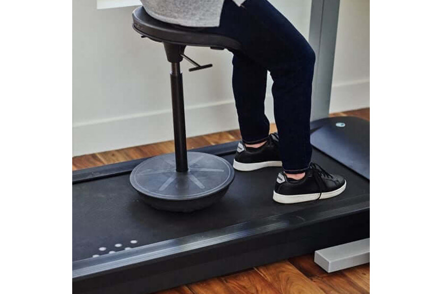 Black and white sneaker worn by model standing on treadmill desk with circular base, adjustable stand, and gray countertop
