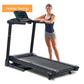 Black folding treadmill with digital console worn by model in navy tank top and gray shorts, on white background