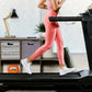 Woman wearing coral pink leggings and white sneakers running on black LifeSpan TR1200i treadmill in home gym setting
