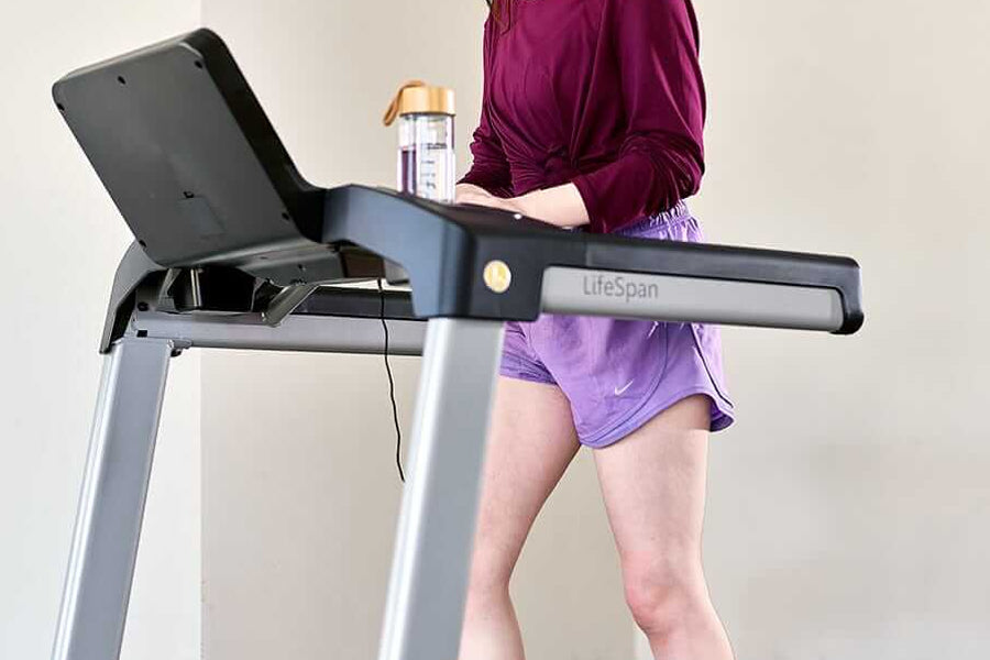 LifeSpan TR3000i folding treadmill with black and silver frame, displayed with model in burgundy jacket and purple shorts