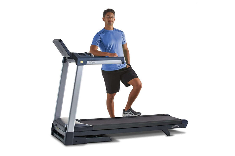 Man wearing blue t-shirt and black shorts running on LifeSpan TR4000i folding treadmill with gray frame and black running dec