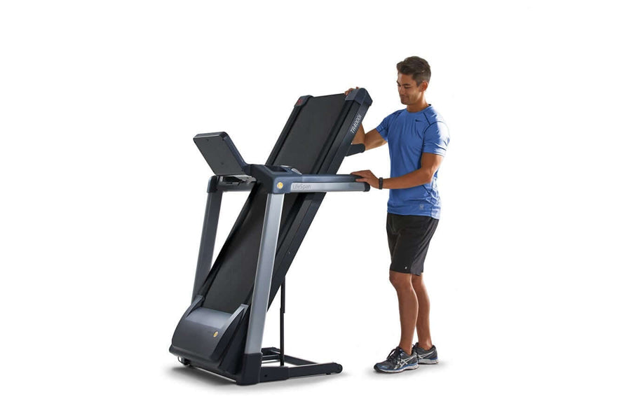 Man in blue shirt using black and gray folding treadmill with digital display on white background