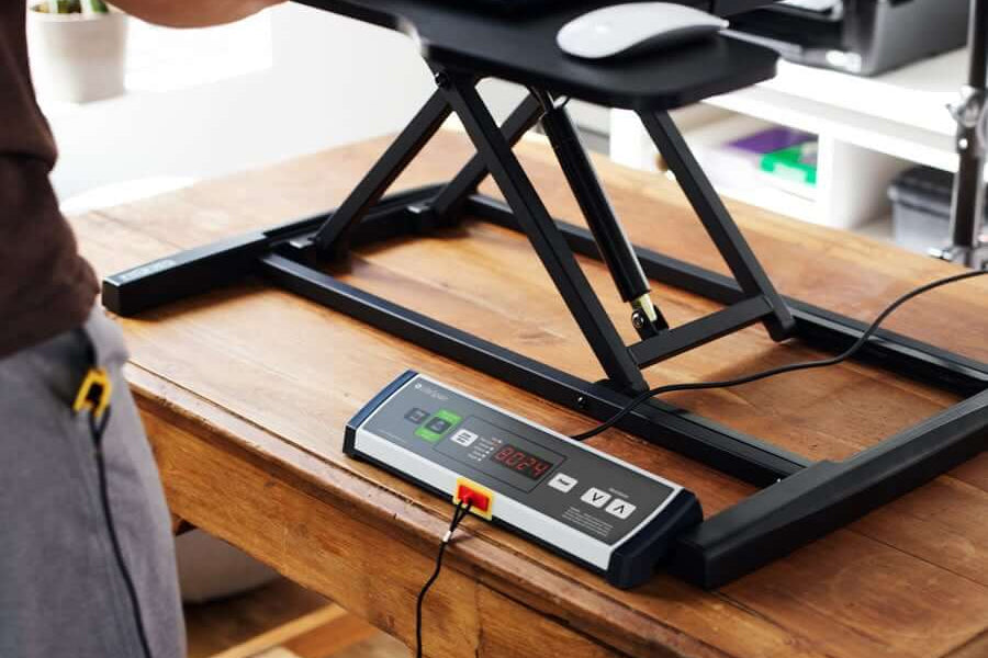 Black under-desk treadmill with digital control panel and folding frame on wooden desk in office setting