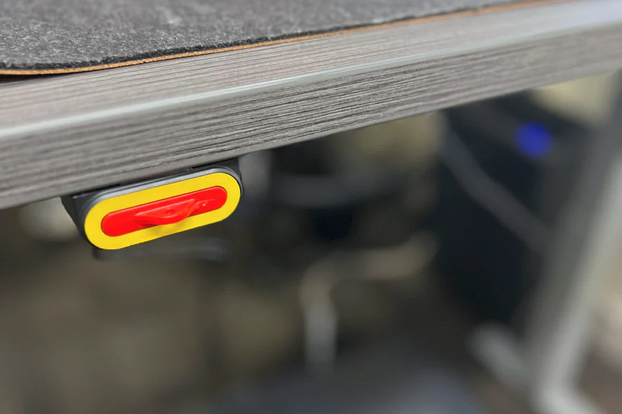 Red and yellow LED indicator light mounted on underside of gray wooden desk frame