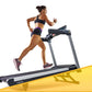 Woman running on LifeSpan TR6000i treadmill with black and gray frame, wearing navy sports bra and purple shorts against whit