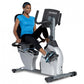 Woman in blue shirt and black leggings using white and black TRUE recumbent exercise bike with digital display on white backg