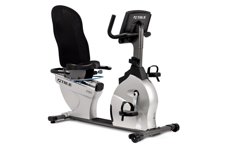 TRUE ES900 recumbent exercise bike with white frame, black seat and handlebars, digital display, and foot pedals on white bac