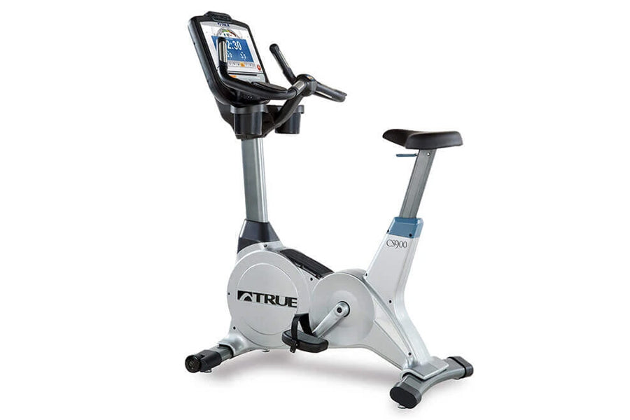 TRUE ES900 upright exercise bike with silver frame, black seat, and digital display console on white background