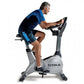 Man wearing blue and black athletic shirt and shorts riding gray TRUE upright exercise bike on white background