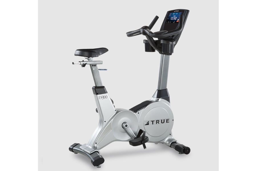 TRUE ES900 upright exercise bike with white and black frame, digital display console, and black padded seat on white backgrou
