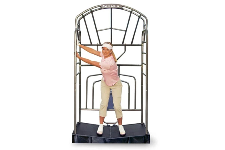 Model wearing pink sleeveless top and beige capris using TRUE Stretch Golf training device with metal frame and black base