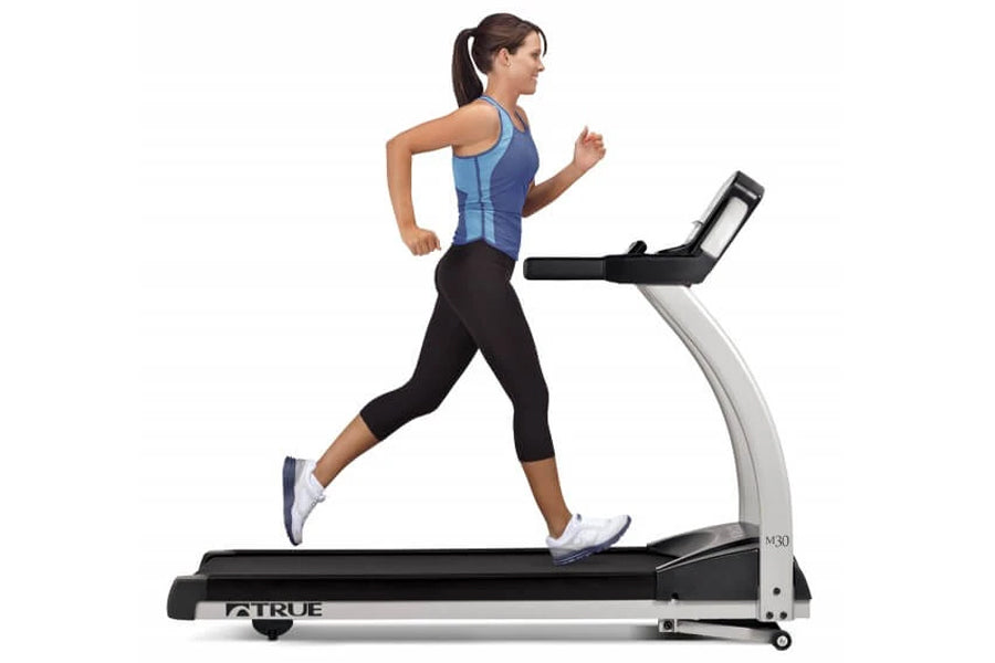 Woman running on TRUE M30 treadmill wearing blue sports tank top and black capri leggings
