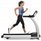 Woman running on TRUE M50 treadmill with blue tank top and black capri leggings, white sneakers, on white background
