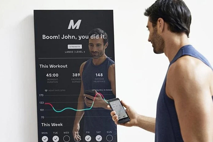 Man in blue tank top viewing lululemon Studio Mirror Pro displaying workout stats and heart rate graph on black screen mounte