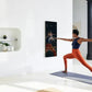 Woman in navy sports bra and orange leggings performing yoga pose in front of black rectangular mirror mounted on white wall