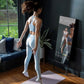 Woman in white sports bra and leggings standing before black interactive fitness mirror in home gym with blue sofa