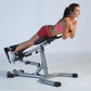 Woman in pink sports top and black shorts using silver hyper-extension bench with leg extension attachment on white backgroun