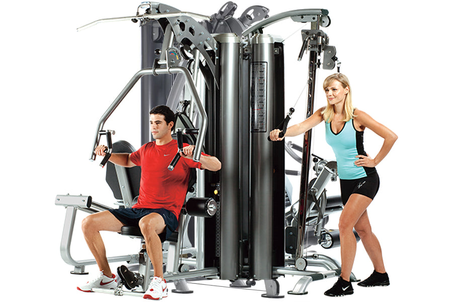 Multi-station gym equipment with gray and black frame featuring three workout stations, demonstrated by man in red shirt seat