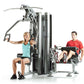 TuffStuff Apollo 7200 2-station multi gym system with woman using chest press and man using leg extension, shown on white bac