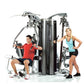 TuffStuff Apollo 7400 4-station multi-gym system with silver metal frame, shown with male model using chest press and female 