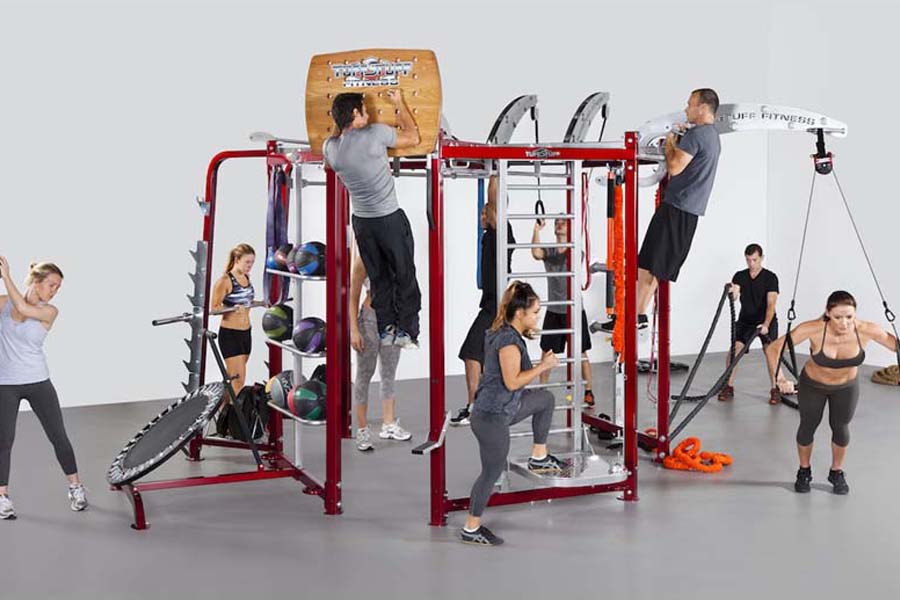 Red metal multi-station fitness training system with various exercise attachments, multiple people using different stations s