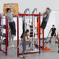 Multiple people using red TuffStuff CT8 multi-station fitness training equipment with pull-up bars, weight storage, and cable