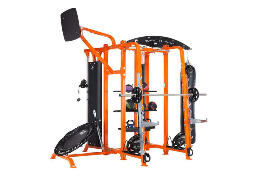 Orange and black multi-station fitness training system with cable machines, weight stack, and attached trampoline on white ba