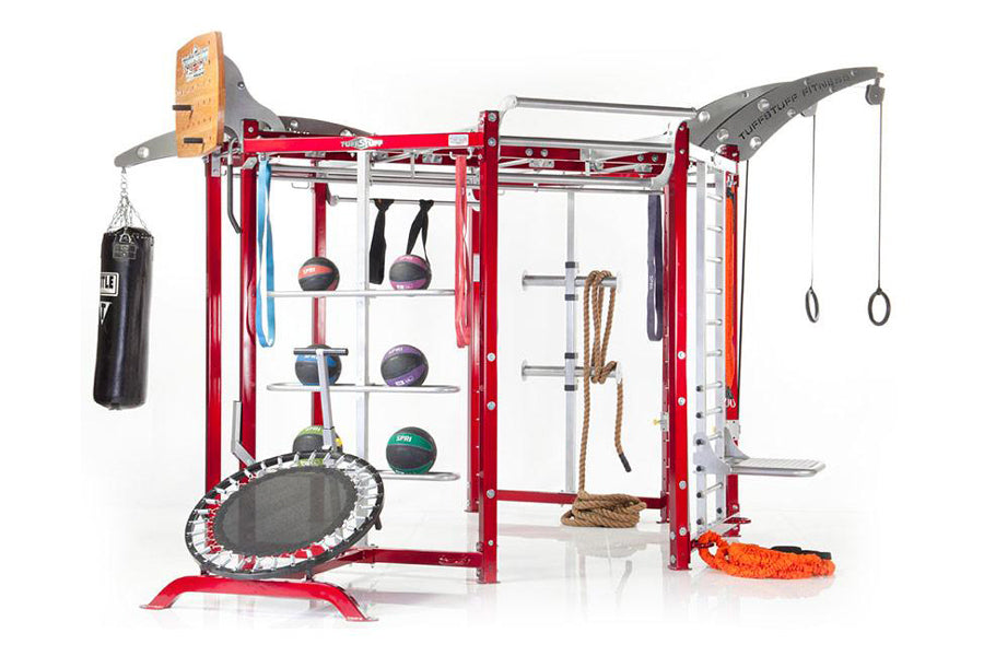 Red and gray multi-functional fitness training rig with integrated pull-up bar, medicine balls, heavy bag, trampoline, and ro