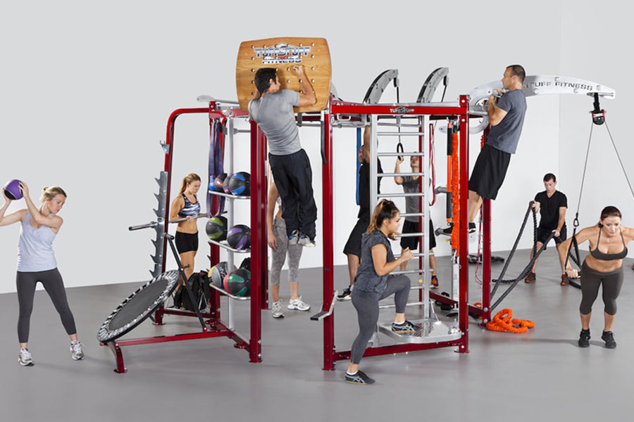Red metal multi-station training rig with multiple users performing various exercises including pull-ups, step-ups, and rope 