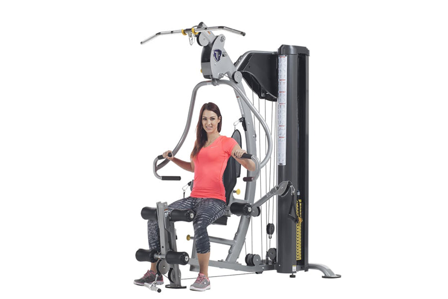 Woman using gray and black multi-station home gym with cable machine and leg press on white background