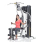 Woman in coral shirt and dark leggings using TuffStuff Classic Home Gym with gray and black frame on white background