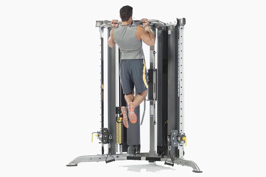 Man performing pull-up on multi-functional trainer with gray frame and black weight stack, on white background